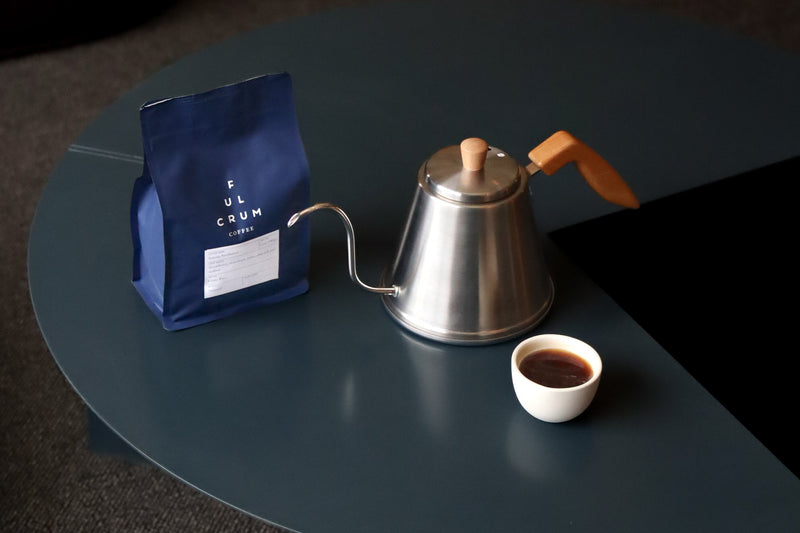 Coffee bag, metal kettle, and small cup on a dark surface