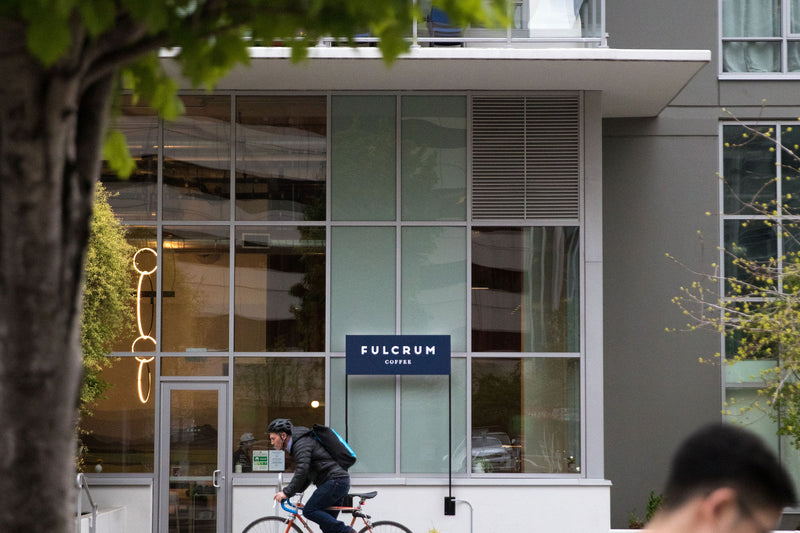Person with a bicycle walking past a modern building with 'Fulcrum' branding.