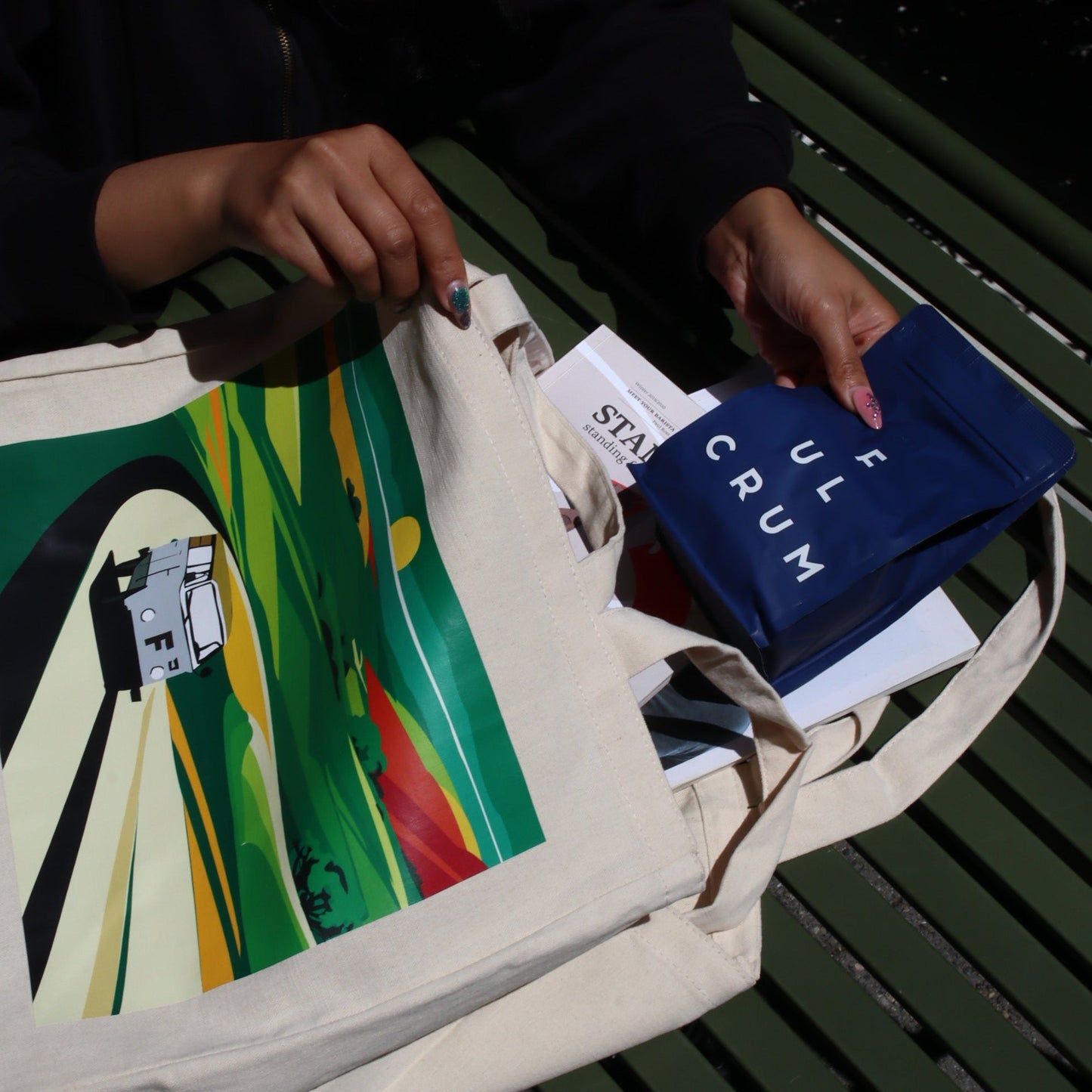Person holding a colorful bag with a book on a green table