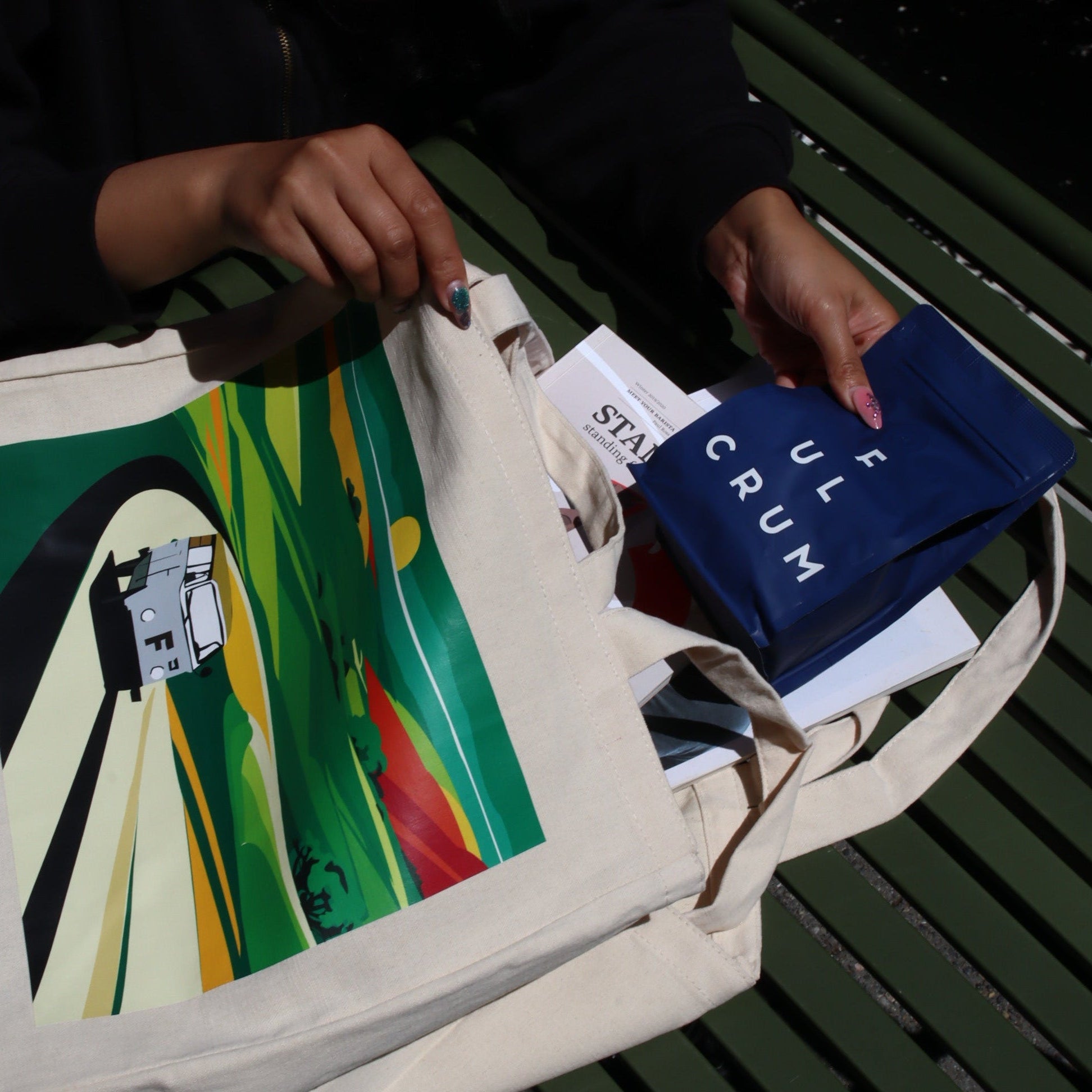Person holding a colorful bag with a book on a green table
