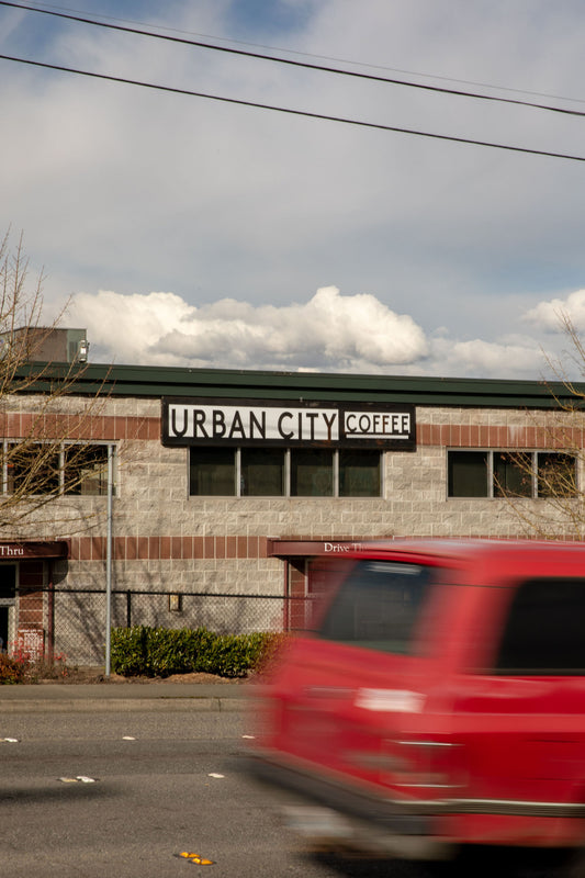 Red van passing by a building with 'Urban City Coffee' sign on a cloudy day.