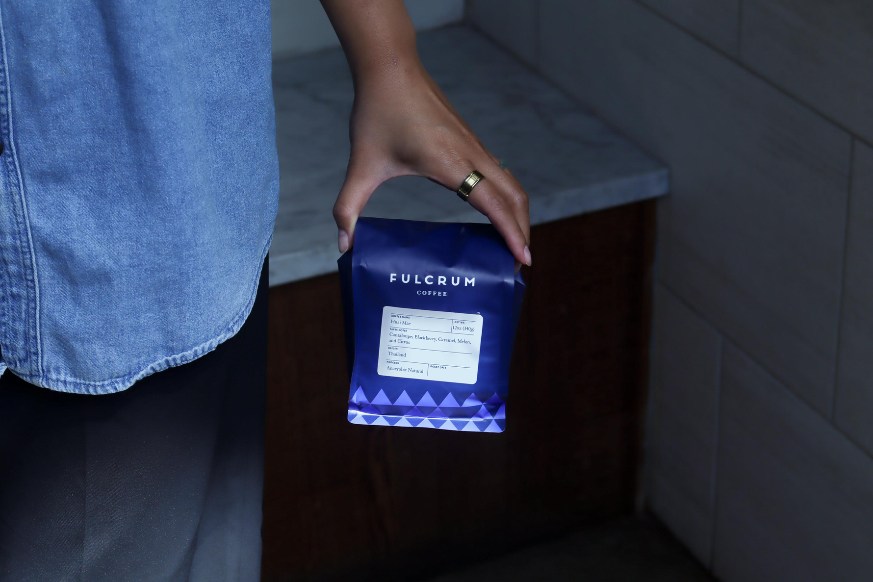 Person holding a Fulcrum coffee package in a kitchen setting